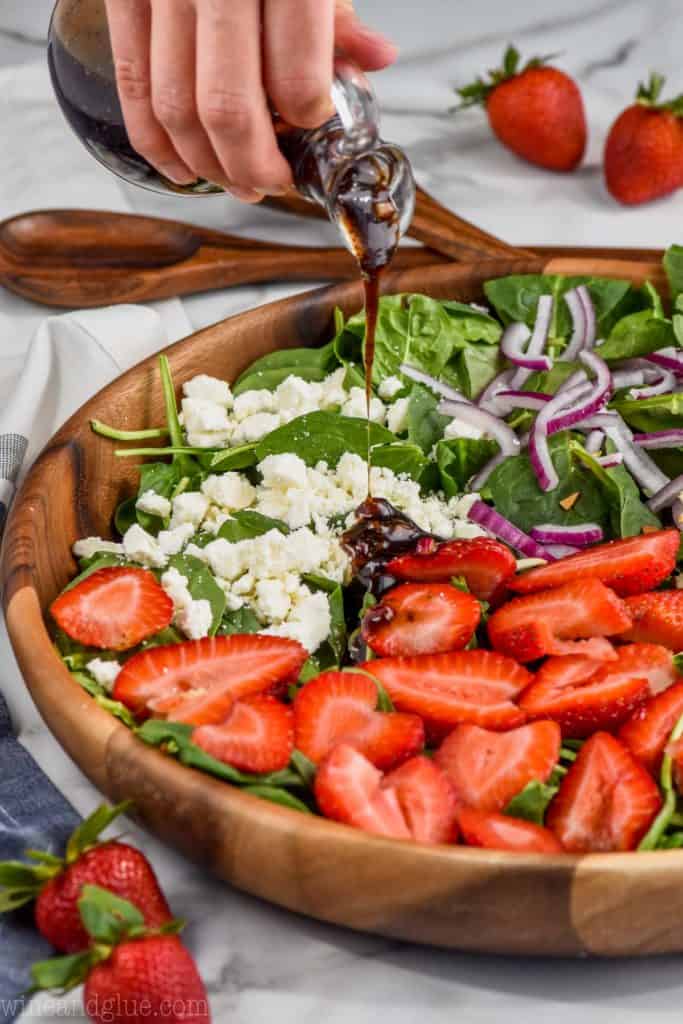 side view of strawberry spinach salad with balsamic poppyseed dressing being poured on it