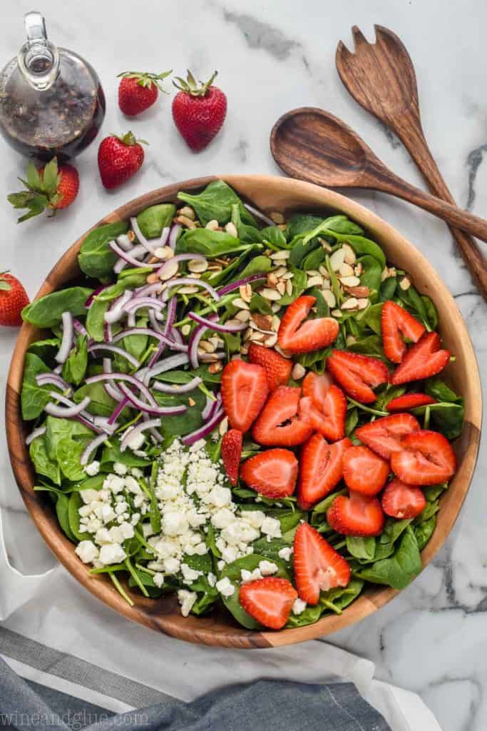 overhead view of spinach strawberry salad with red onions, toasted almonds, and feta cheese