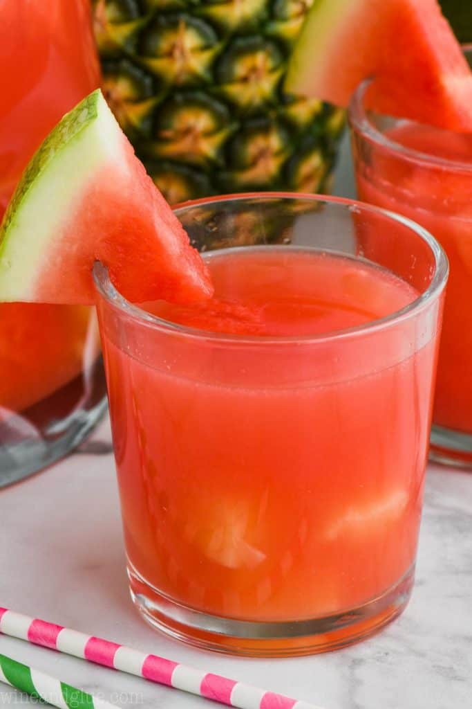 small tumbler filled with bright red watermelon rum punch with pineapple chunks and garnished with a watermelon slice