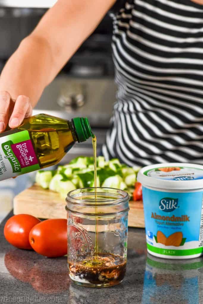 woman pouring olive oil into a mason jar to make creamy balsamic dressing