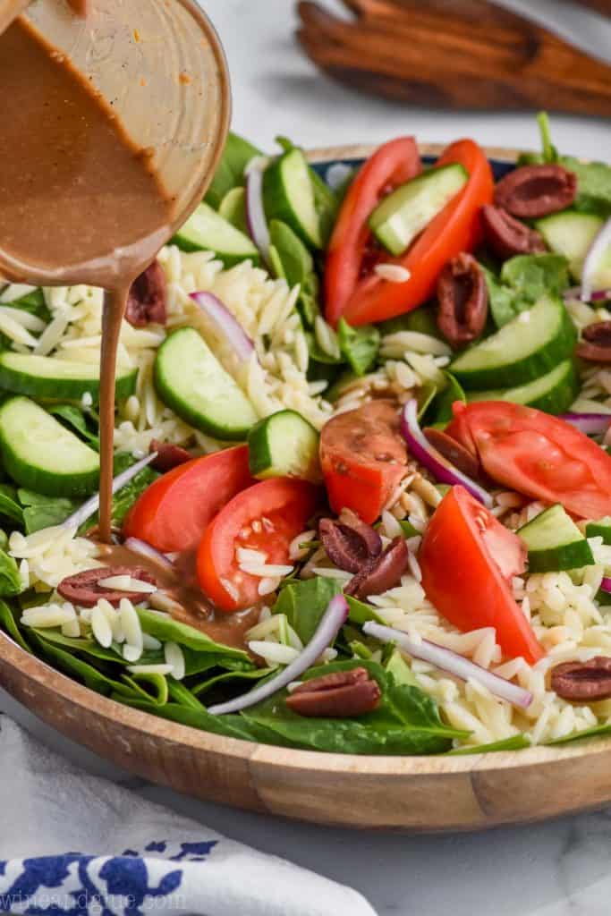 bowl of orzo pasta salad with creamy balsamic dressing being poured over it.