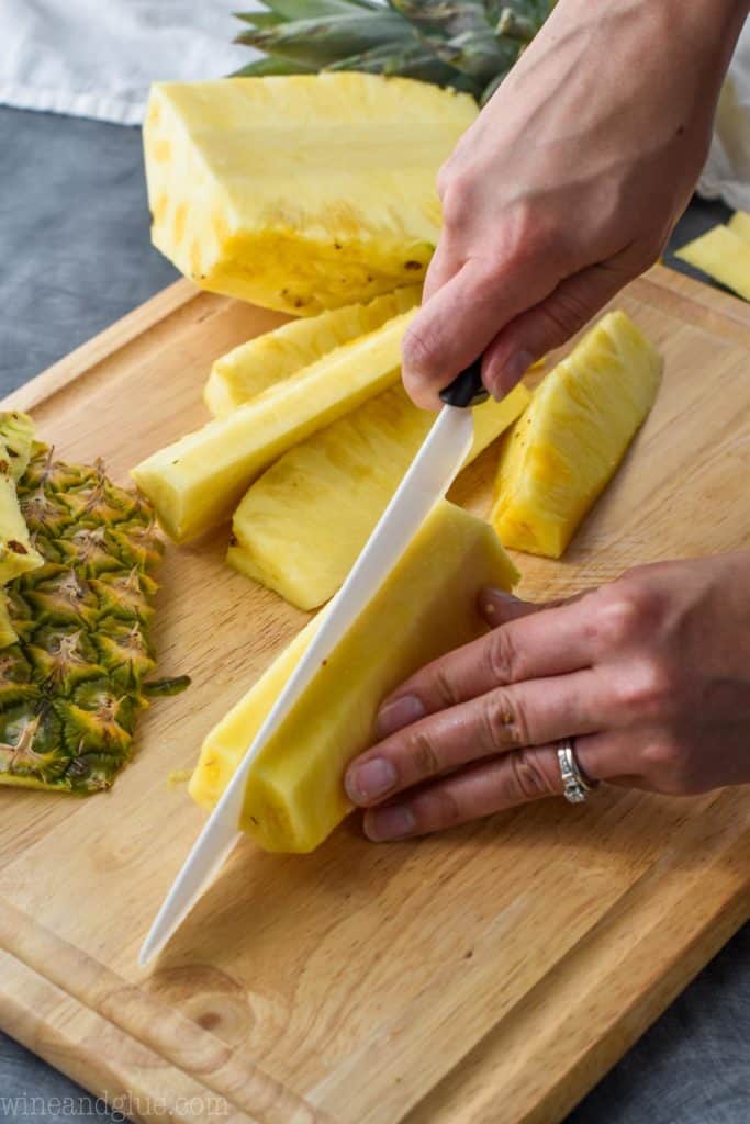 a pineapple being cut into spears on a cutting board