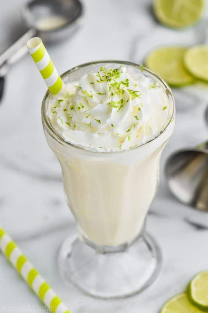 overhead view of a boozy margarita milkshake with a stripped straw and garnished with lime zest