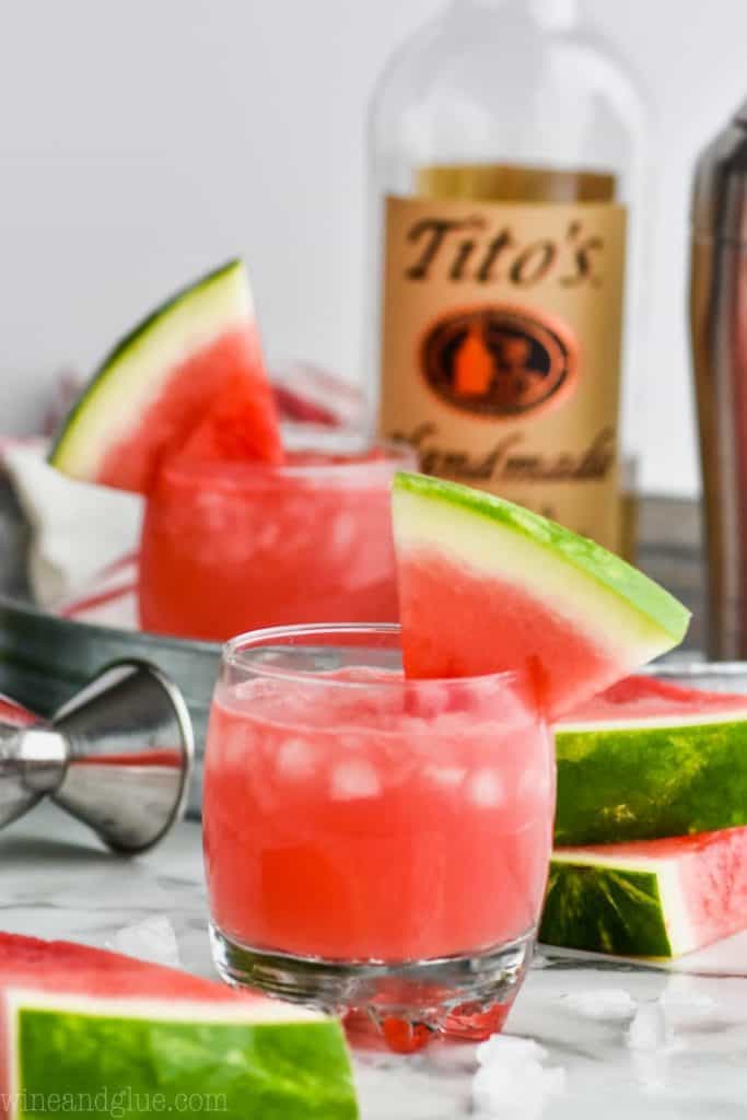 small tumbler of watermelon vodka tonic cocktail with bottle of titos in the background 