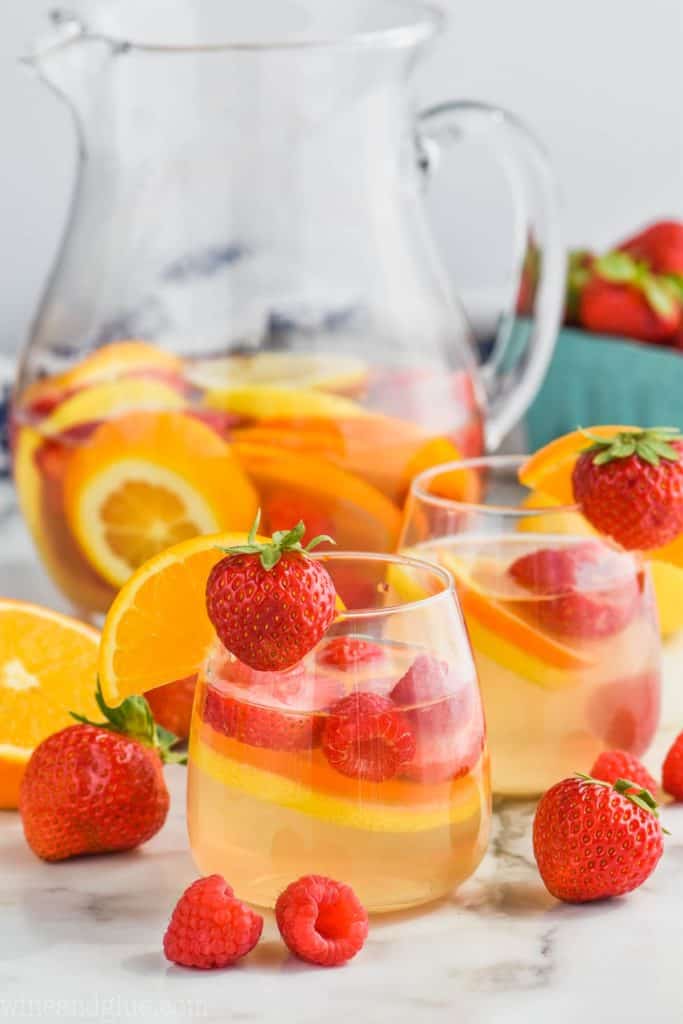 glass of white wine sangria recipe with strawberries and oranges with pitcher behind