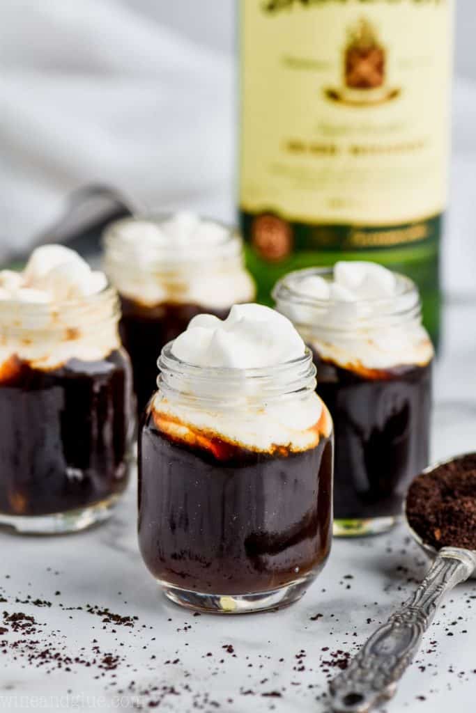 four irish coffee shots topped with whipped cream with a bottle of jameson whiskey in the background