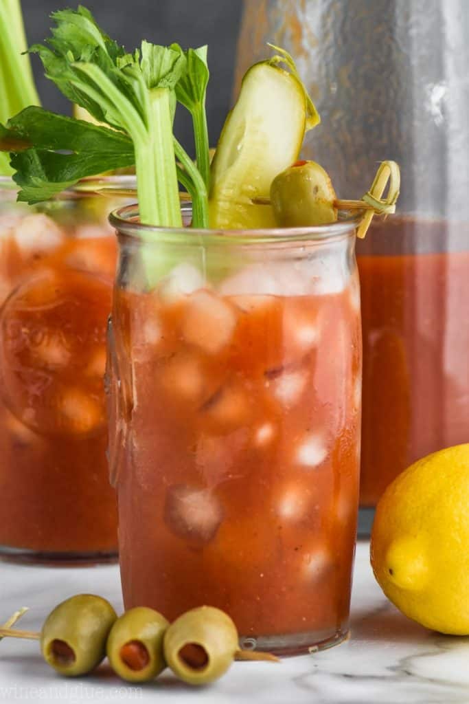 a glass of bloody mary mix recipe garnished with celery, pickle, and olives