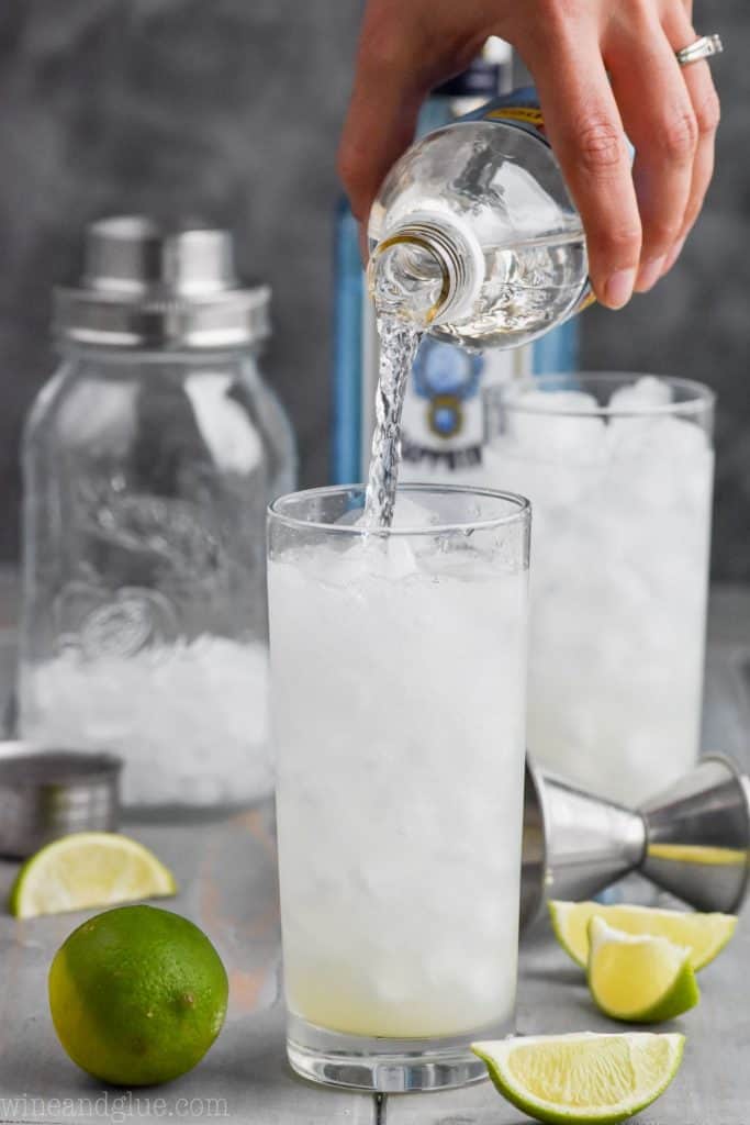 pouring club soda into a glass of gin rickey drink