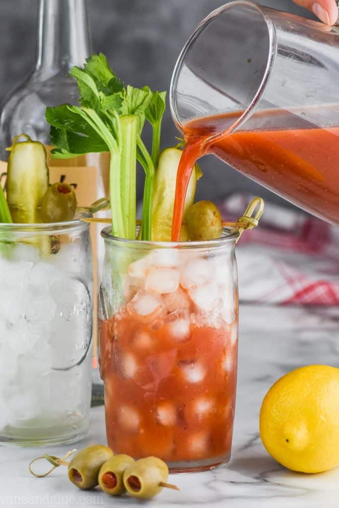 pouring homemade bloody mary mix into a glass of ice thats garnished