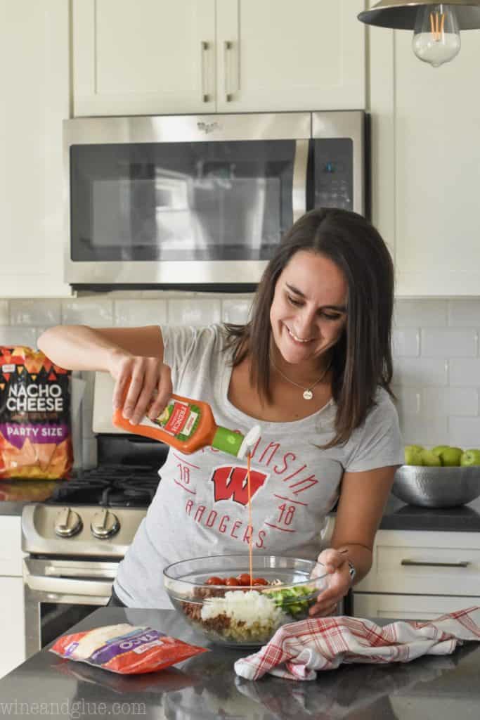 woman pouring french dressing into taco pasta salad