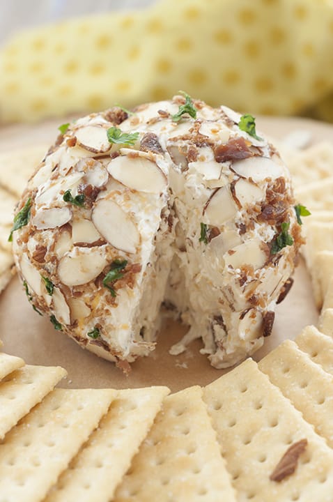 The Buttermilk Ranch Bacon Cheese Ball is in the middle of the plate surrounded by Club Crackers and has a small slice cut out. 