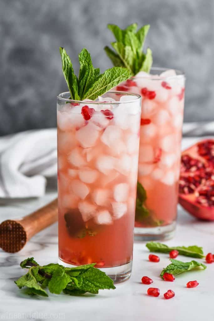 Two Pomegranate Mojitos with crushed ice and chunks of pomegranate and topped with mint leaves. 