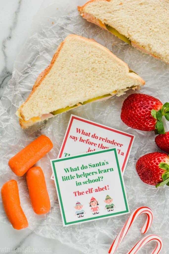 two christmas lunch box jokes with a sandwich, carrots, and strawberries