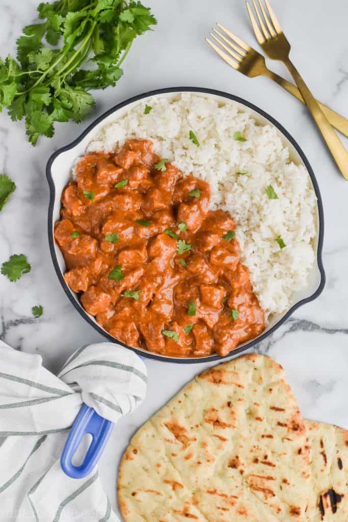 pan of creamy butter chicken with rice, cilantro and naan