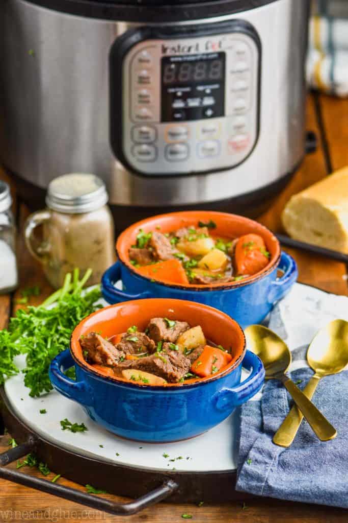 two bowls of instant pot beef stew with pressure cooker in background