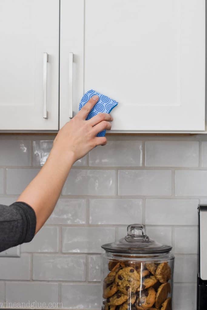 woman using a sponge to clean grease off cabinets 