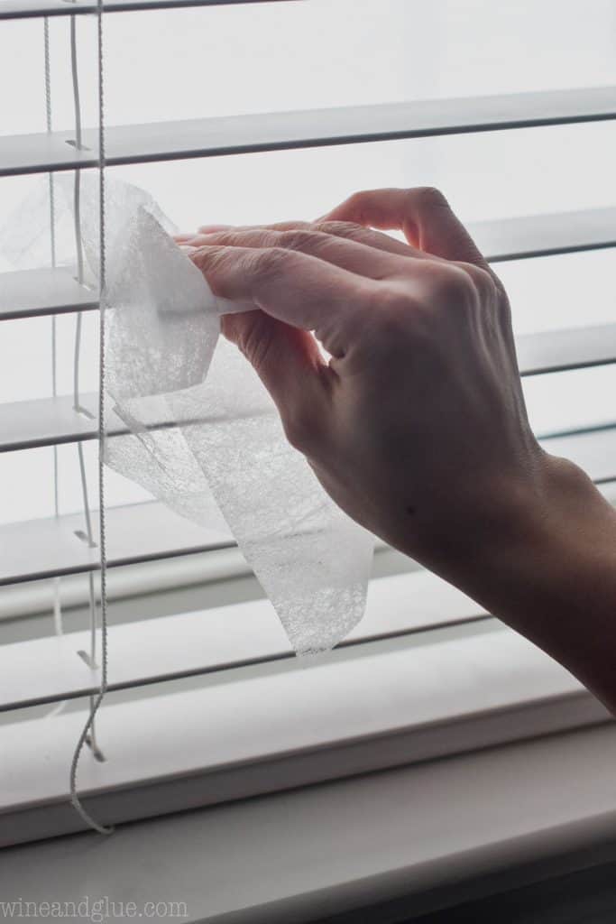 woman using a dryer sheet to clean blinds