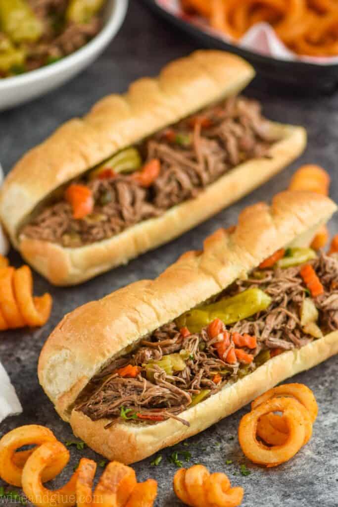 two italian beef sandwiches with curly fries around them on a granite surface