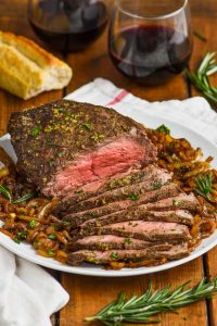 easy top round roast beef recipe garnished with fresh herbs and on a plate of caramelized onions