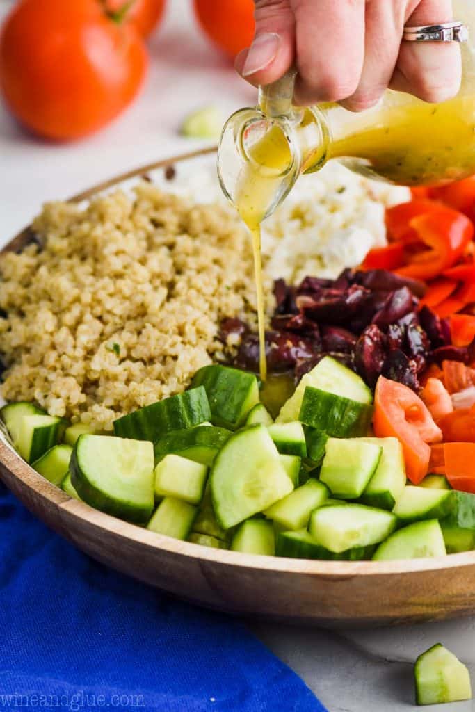 pouring greek salad dressing on greek quinoa salad