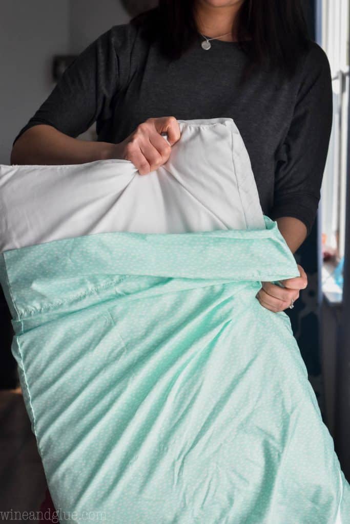 woman pulling a pillow out of a pillow case to clean a ceiling fan