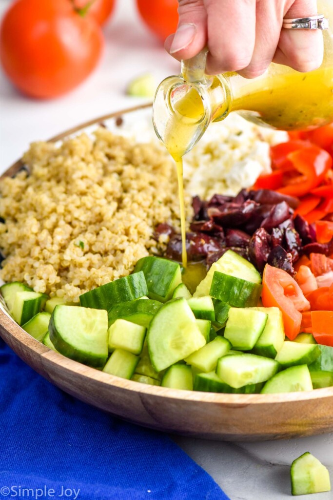 pouring greek salad dressing on greek quinoa salad