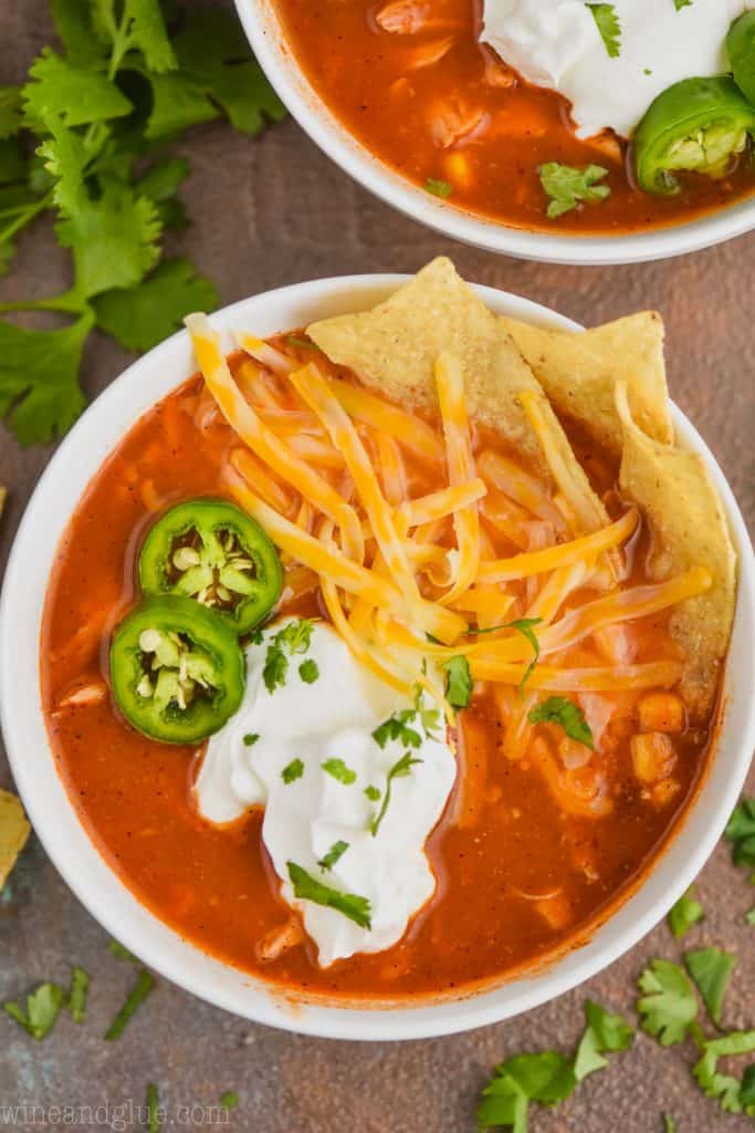 close up overhead view of a bowl of slow cooker chicken tortilla soup recipe that has been garnished with sour cream, sliced jalapeÃ±os, shredded cheese, and tortilla chips