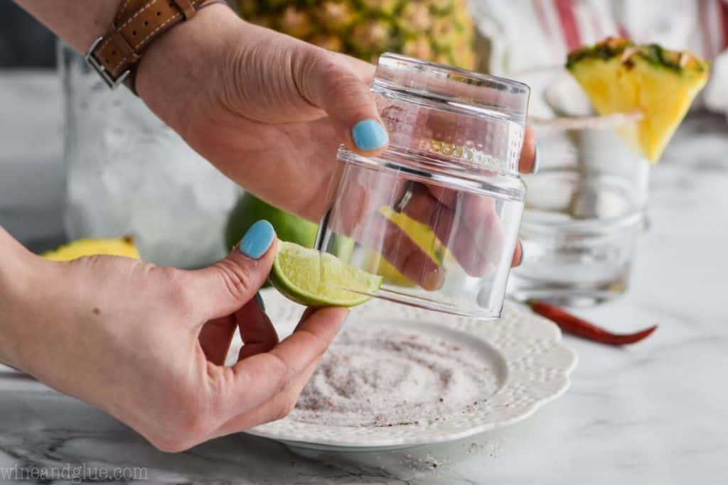 woman's hands rubbing a lime wedge around an upside down glass