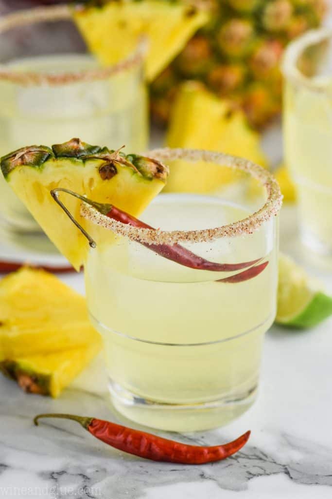a glass of pineapple margarita garnished with a pineapple wedge and a chile pepper