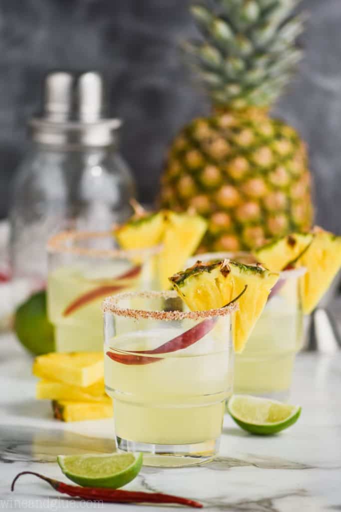 three glasses of pineapple margaritas garnished with pineapple wedges and red chile peppers