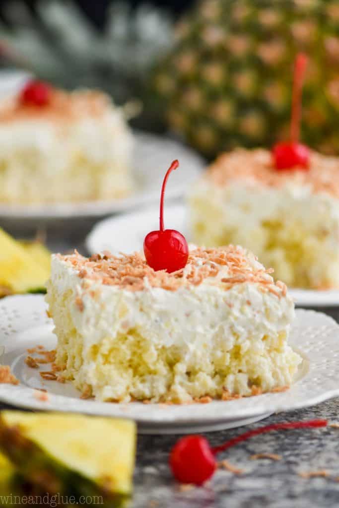 piece of pina colada poke cake topped with toasted coconut and cherry on a white plate