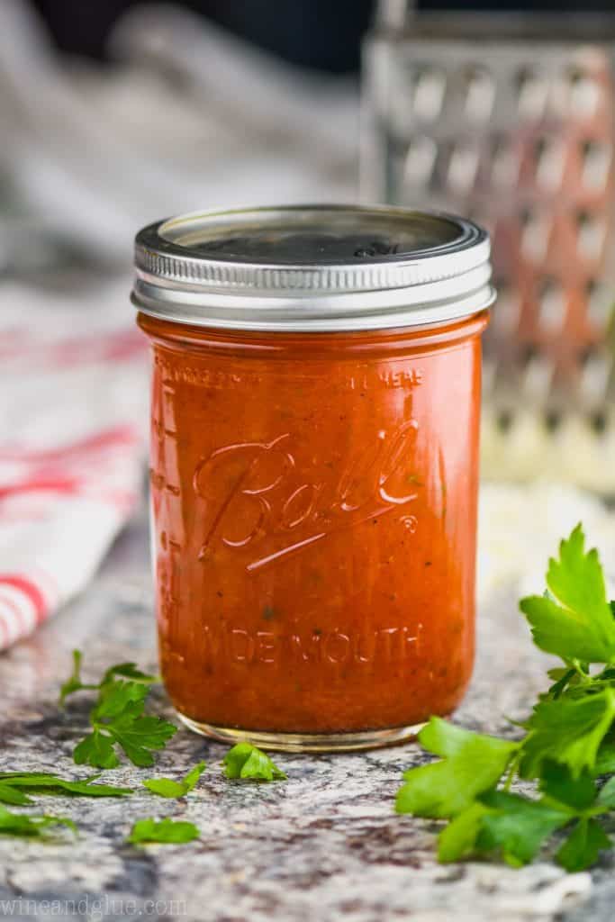 homemade pizza sauce in a widemouth ball jar with a cheese grater in the background and fresh parsley in the foreground