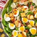 overhead view of spinach bacon salad with hard boiled eggs, croutons, water chestnuts in a white bowl