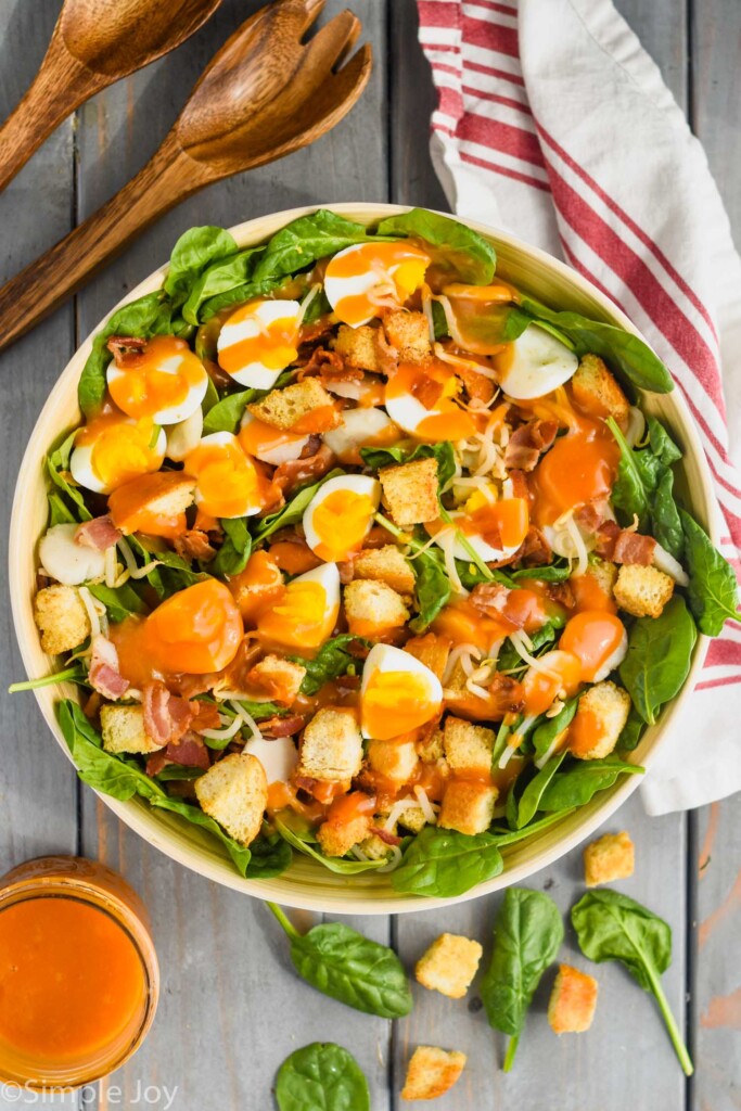 overhead of a spinach salad with bacon in a large bowl covered with dressing 