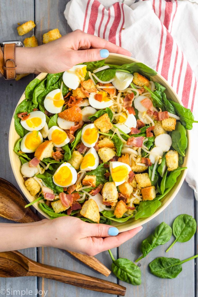 two hands holding a white salad bowl filled with the best spinach salad recipe