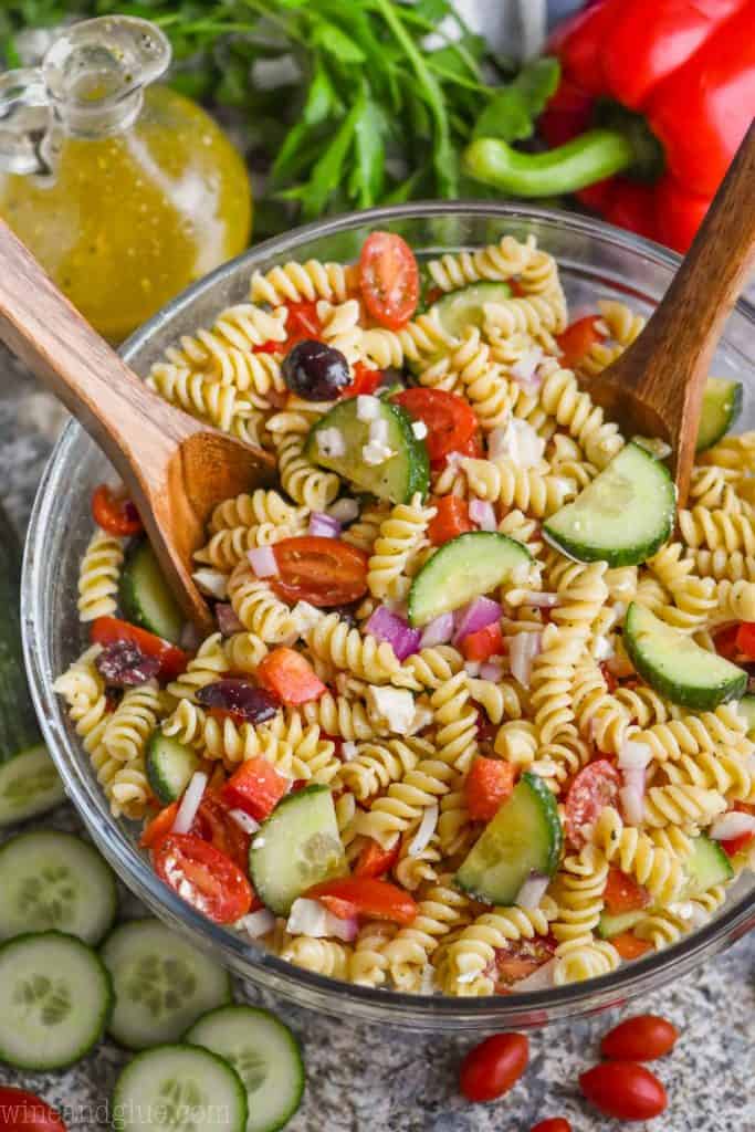 overhead view of greek pasta salad in a bowl with wooden spoons