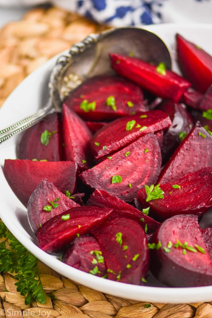 white bowl full of roasted beets recipe and antique spoon, garnished with fresh parsley