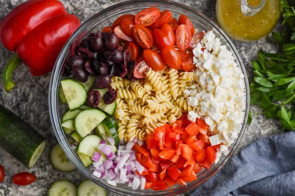 overhead view of greek pasta salad ingredients separated out in a bowl