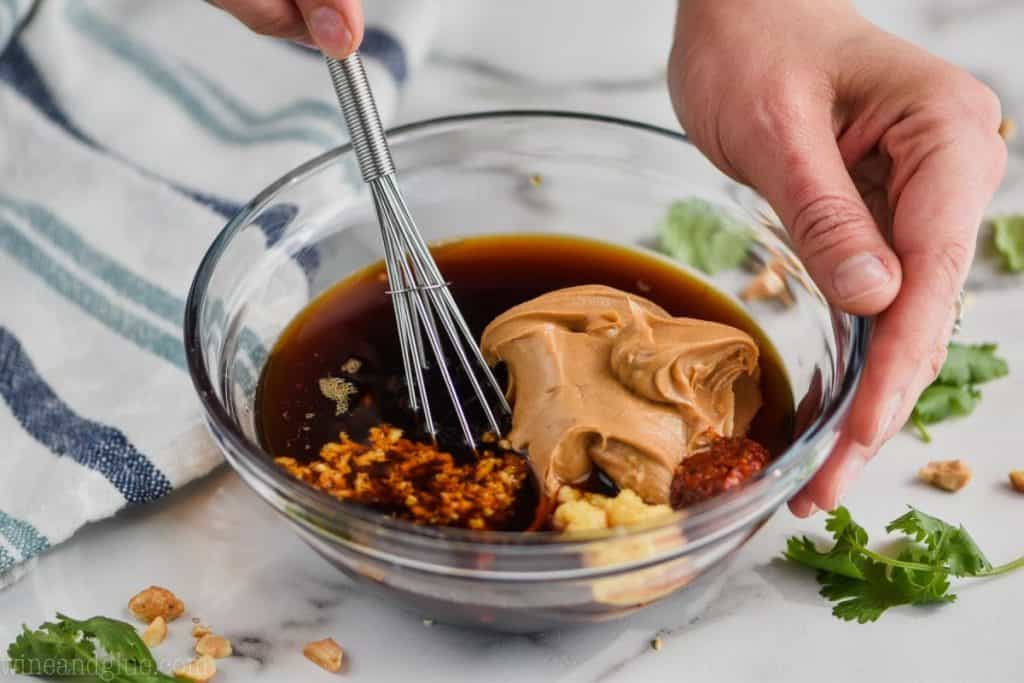 a small bowl with ingredients or peanut sauce in it being whisked by a tiny whisk