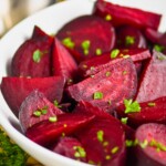 a white bowl on a wood mat filled with wedges of roasted beets sprinkled with parsley