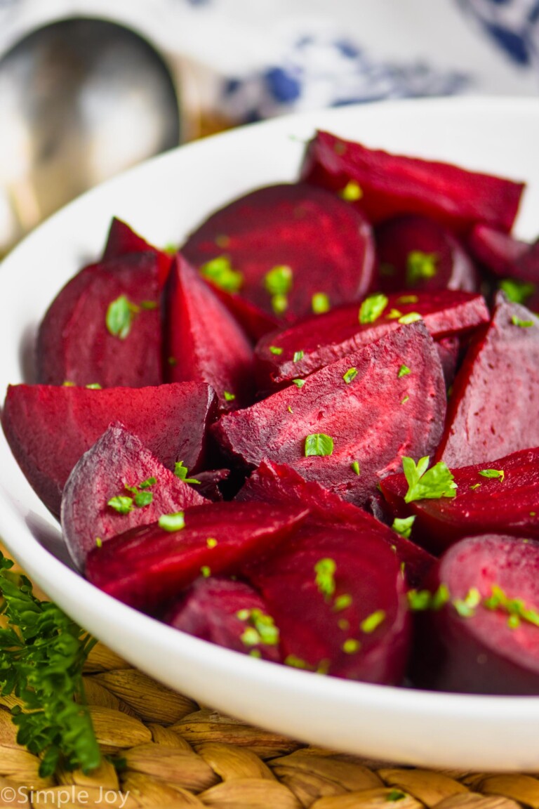 a white bowl on a wood mat filled with wedges of roasted beets sprinkled with parsley