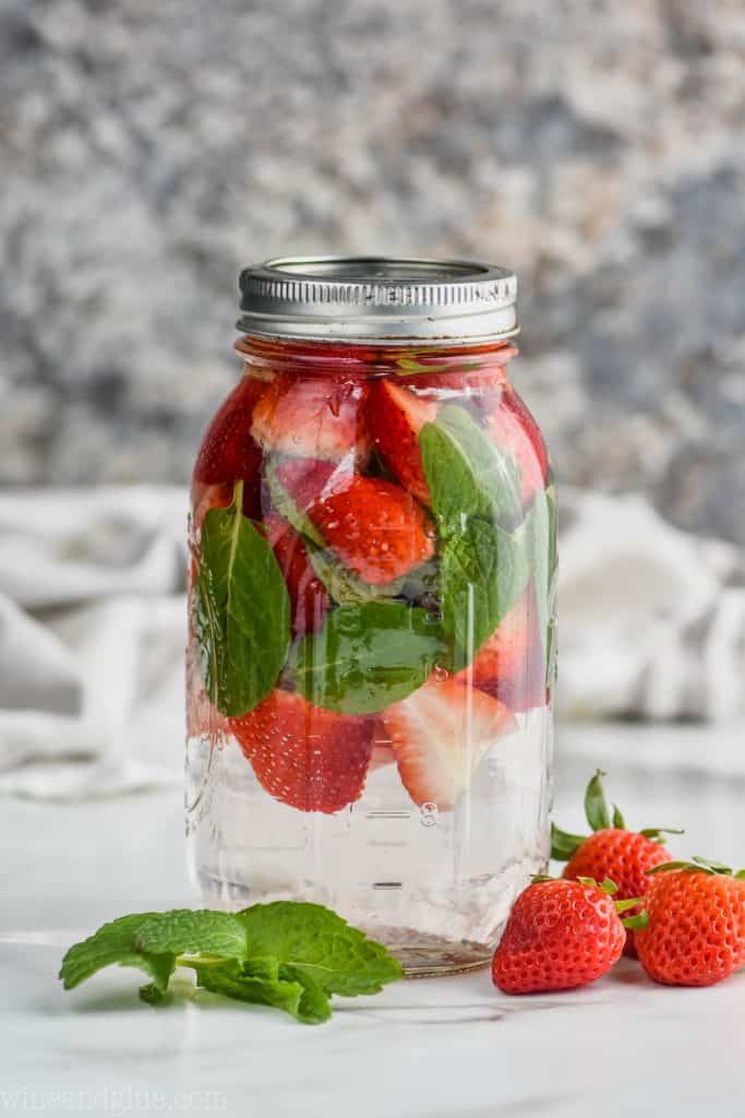mason jar full of cut strawberries and fresh mint leaves to make infused water