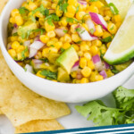 pinterest graphic of small white bowl of corn salsa with two lime wedges, says: the best corn salsa simplejoy.com