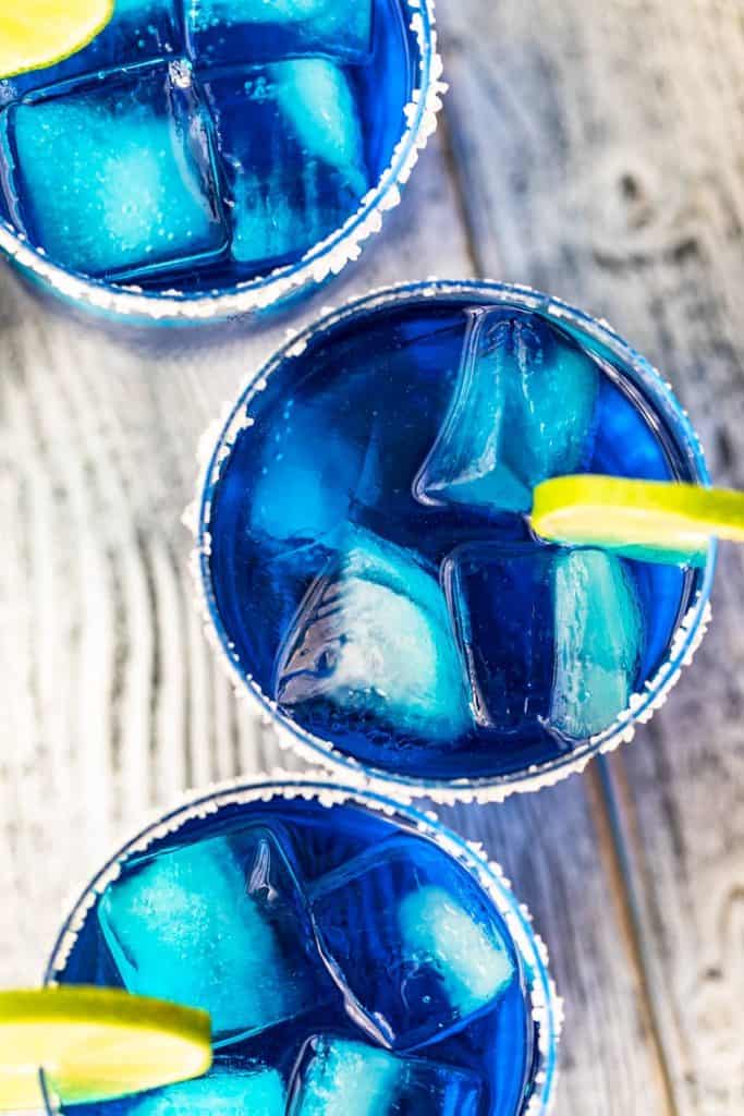 overhead view of three tumblers filled with blue azul margaritas and rimmed with salt