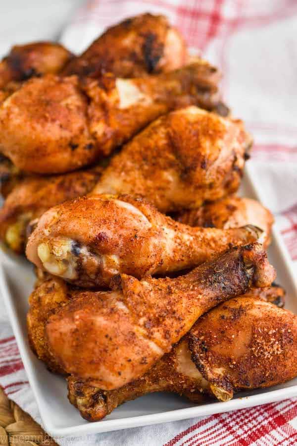 pile of chicken legs that have been grilled with dry chicken rub on a white plate sitting on a red striped napkin