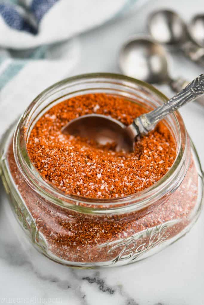 small mason jar filled of chicken rub mix with measuring spoon in it on a white marble counter