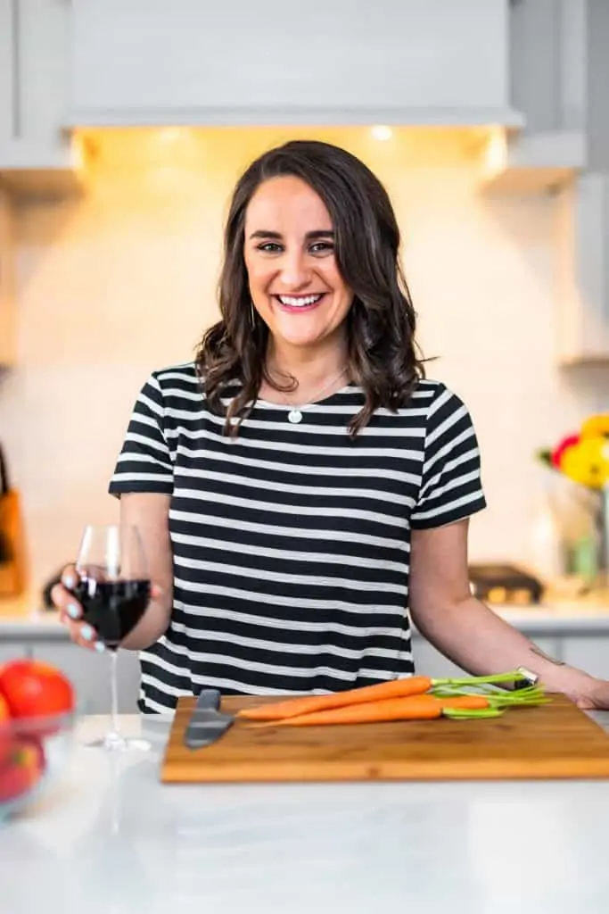 picture of lisa longley, author of simple joy, in a kitchen holding a wine glass with a cutting board in front of her