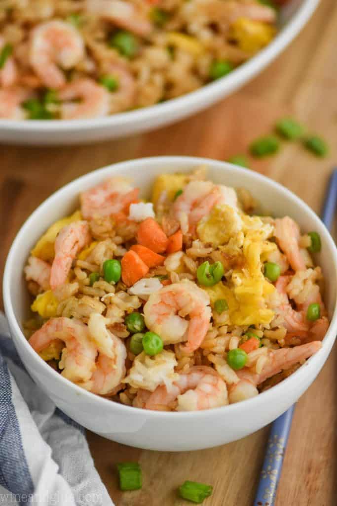 small white bowl filled with shrimp fried rice recipe on a cutting board with a cloth napkin next to it