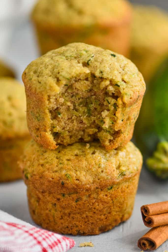 a zucchini muffin that is missing a bites stacked on top of another zucchini muffin with a red and white cloth napkin visible on a gray surface