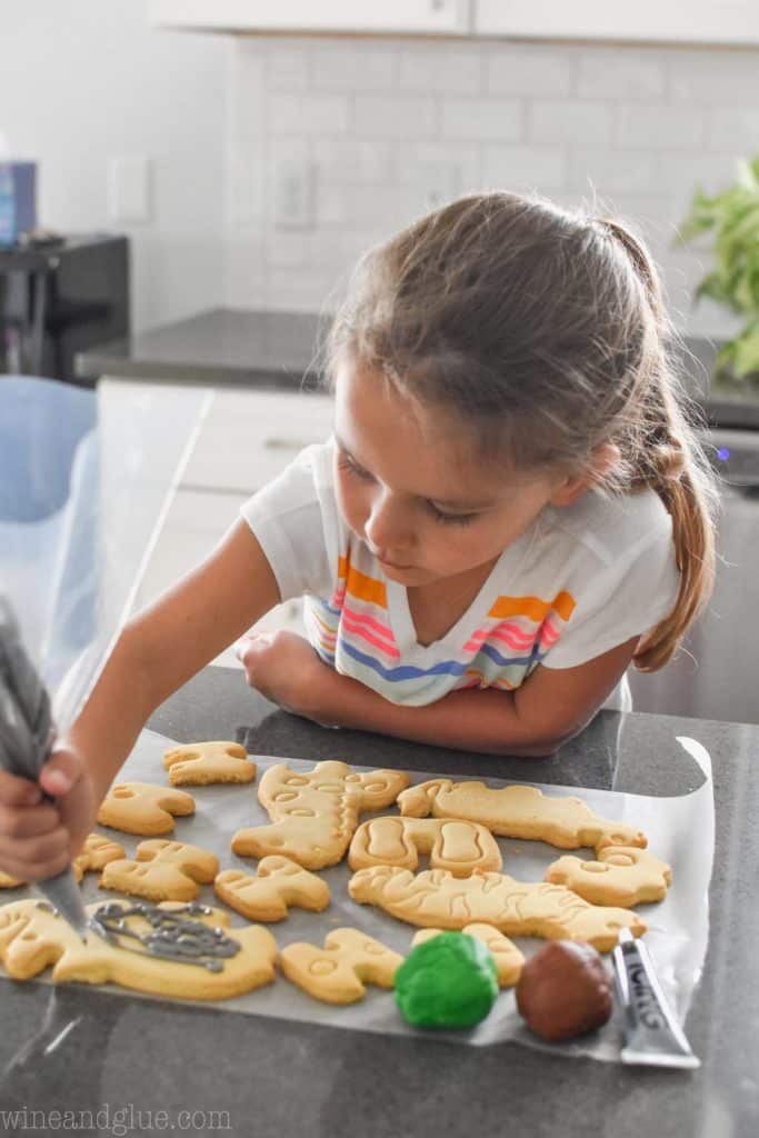 little girl piping gray frosting on an elephant cookie